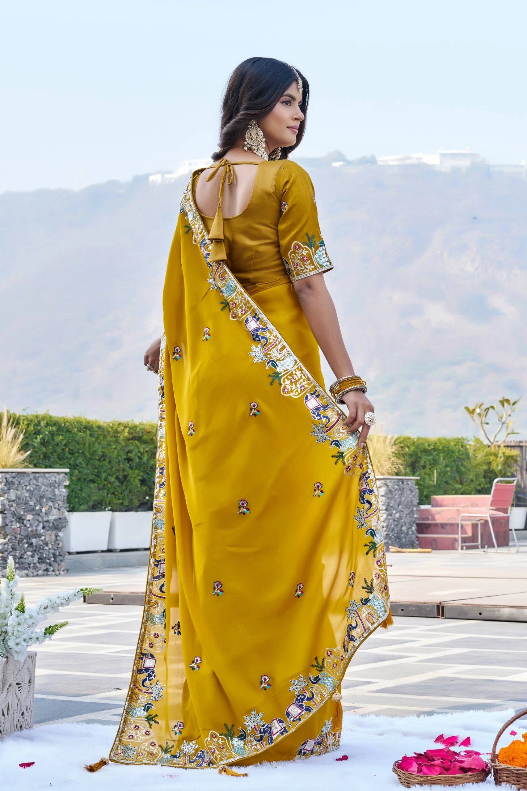 Woman in a yellow saree with floral patterns standing outdoors.